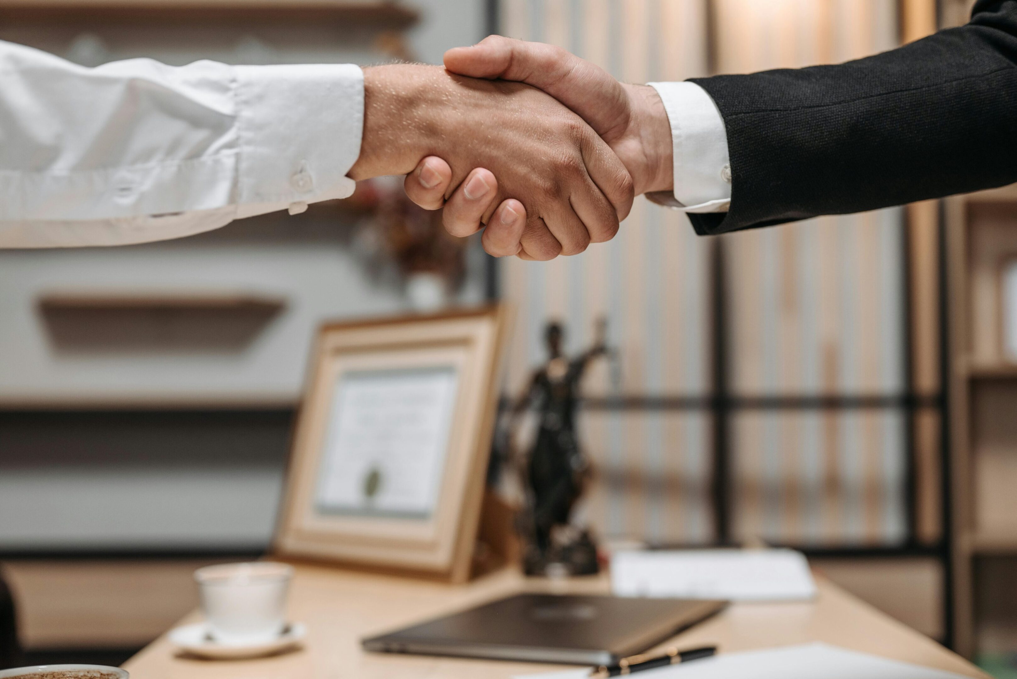 Two people shaking hands over a desk